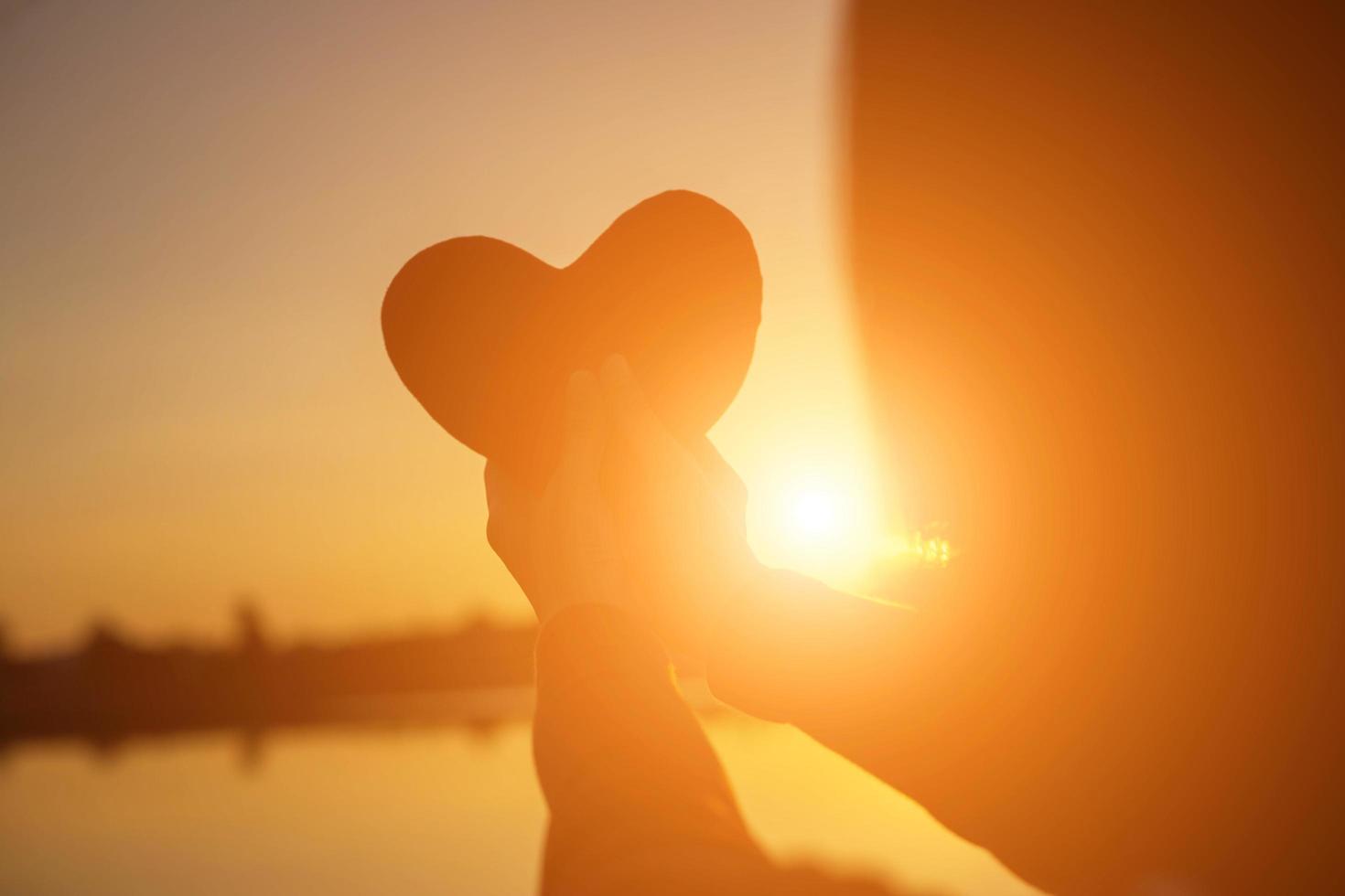 hands forming a heart shape with sunset silhouette photo