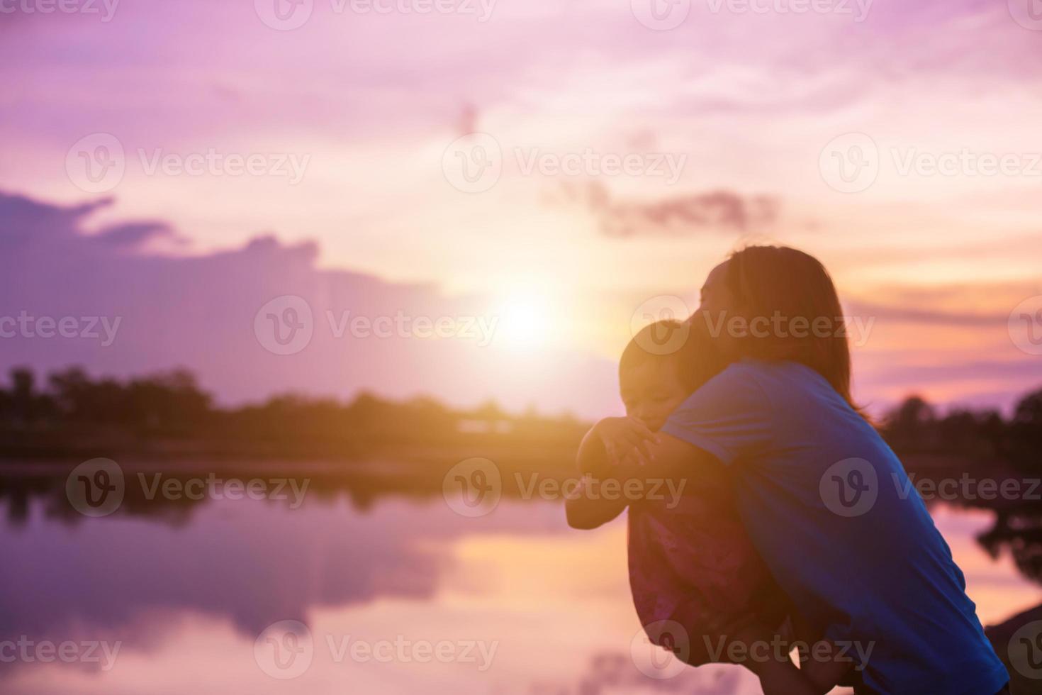 a silhouette of a happy young girl child the arms of his loving mother for a hug, in front of the sunset in the sky on a summer day. photo