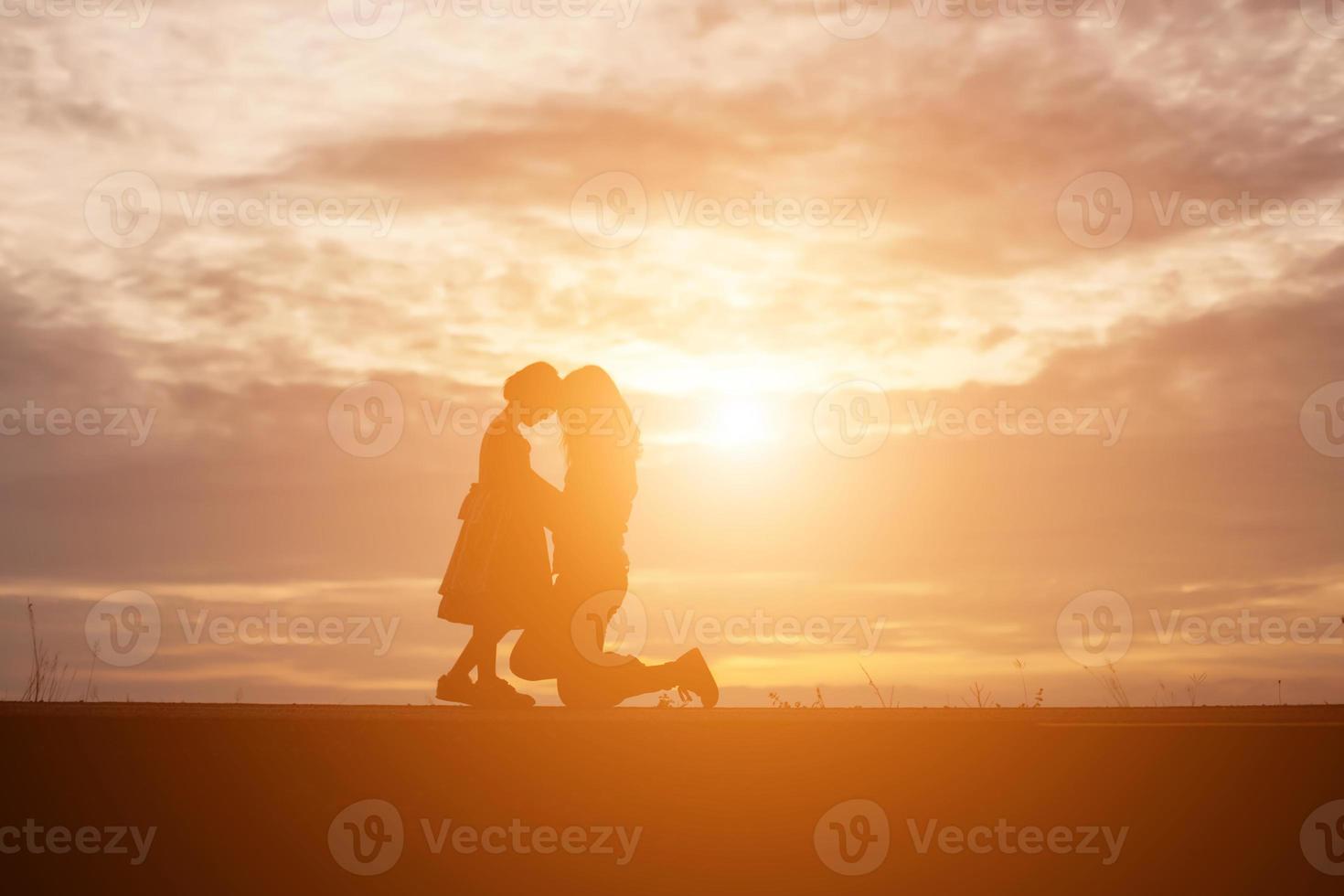 a silhouette of a happy young girl child the arms of his loving mother for a hug, in front of the sunset in the sky on a summer day. photo