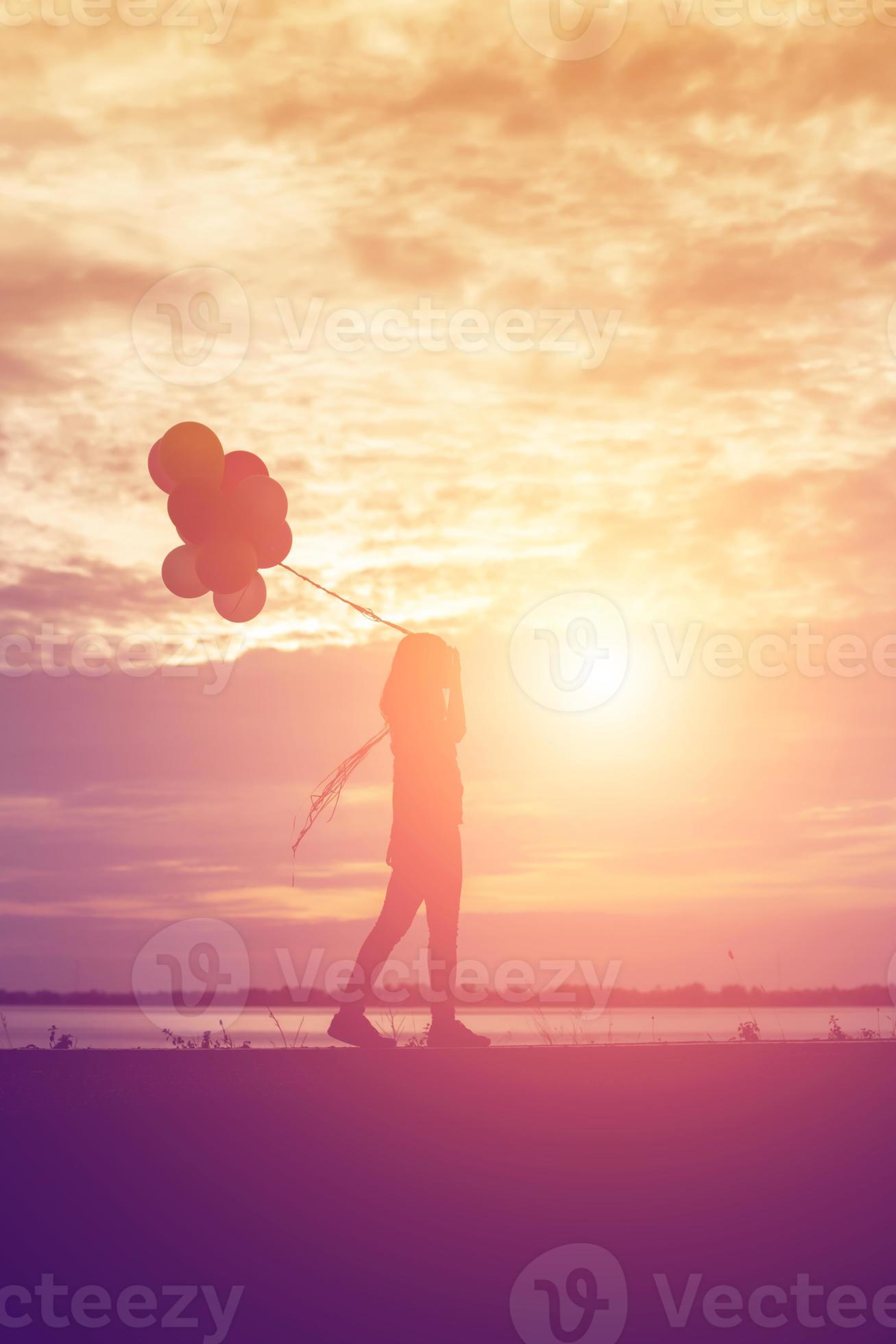 silhouette of young woman holding colorful of balloons with sunset ...