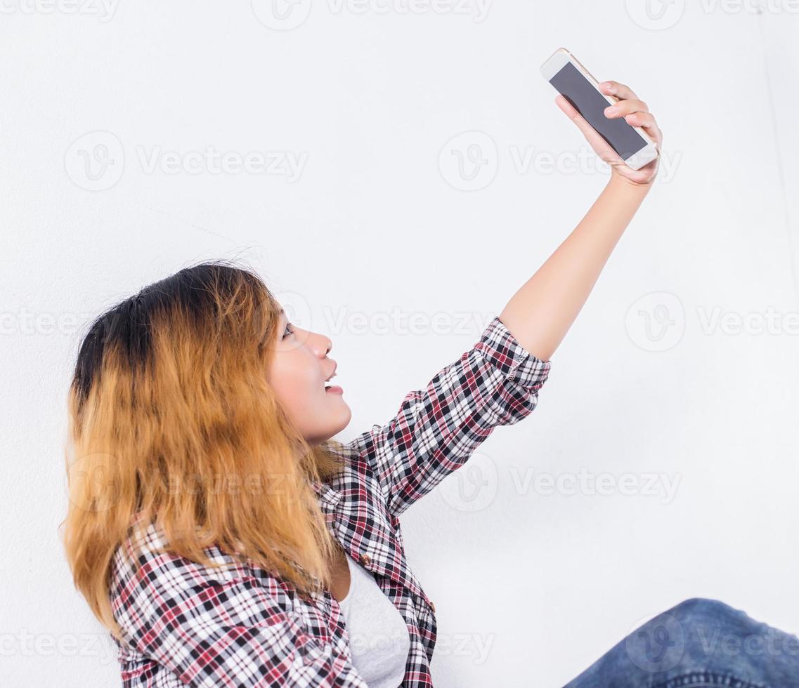 Happy young hipster woman taking selfie photo on smartphone over white background.