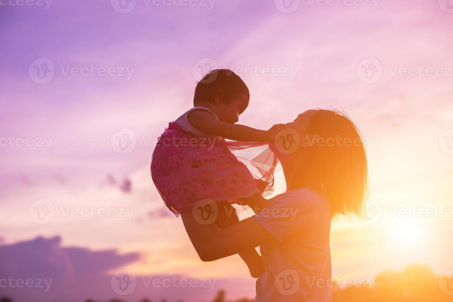 a silhouette of a happy young girl child the arms of his loving mother for a hug, in front of the sunset in the sky on a summer day. photo