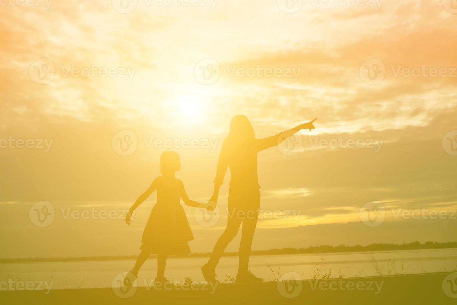 a silhouette of a happy young girl child the arms of his loving mother for a hug, in front of the sunset in the sky on a summer day. photo