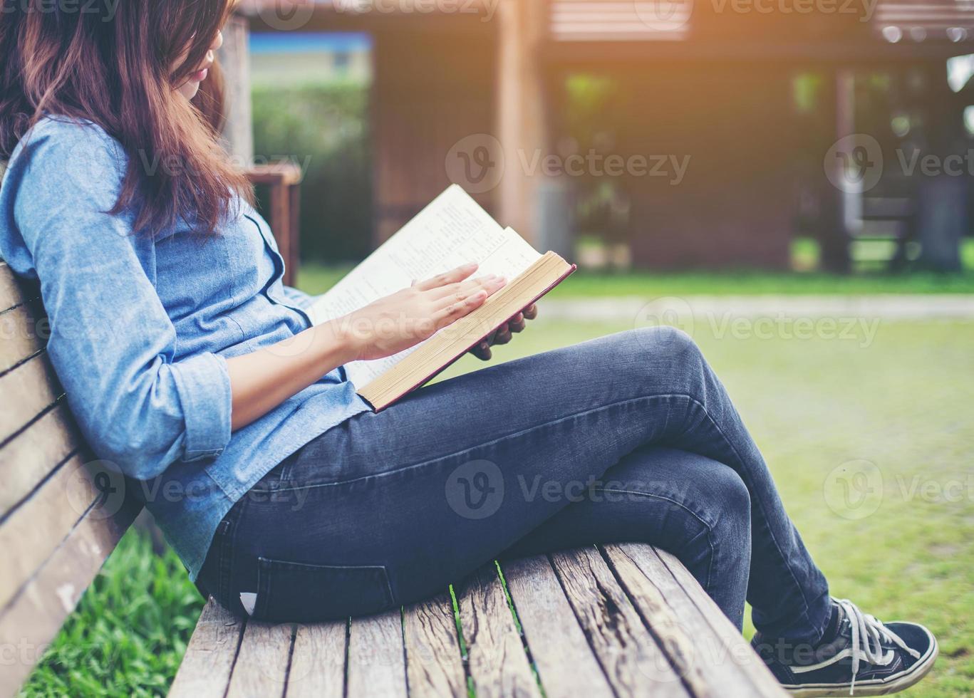 Hipster charming girl relaxing in the park while read book, Enjoy nature around. photo
