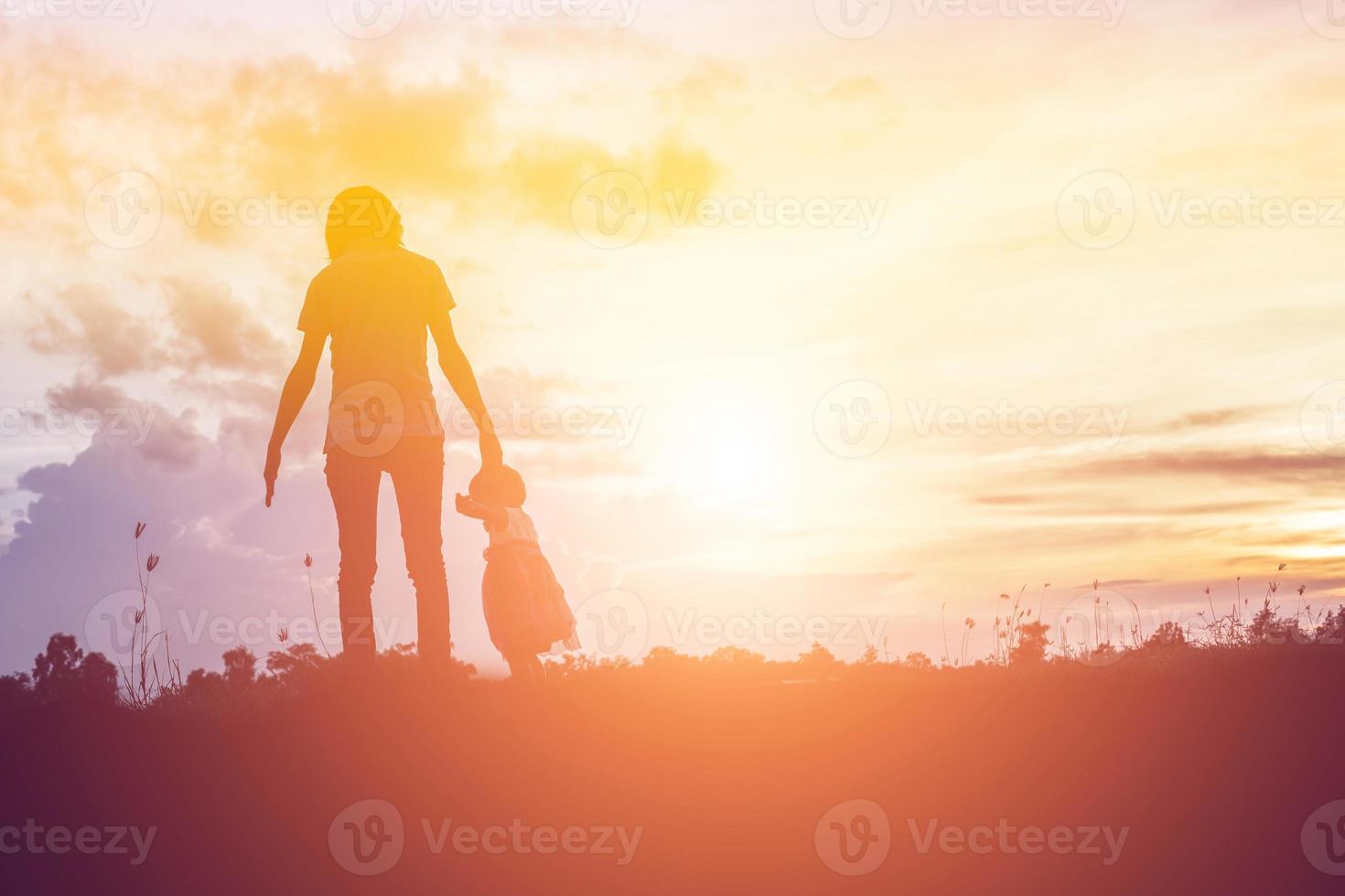 a silhouette of a happy young girl child the arms of his loving mother for a hug, in front of the sunset in the sky on a summer day. photo