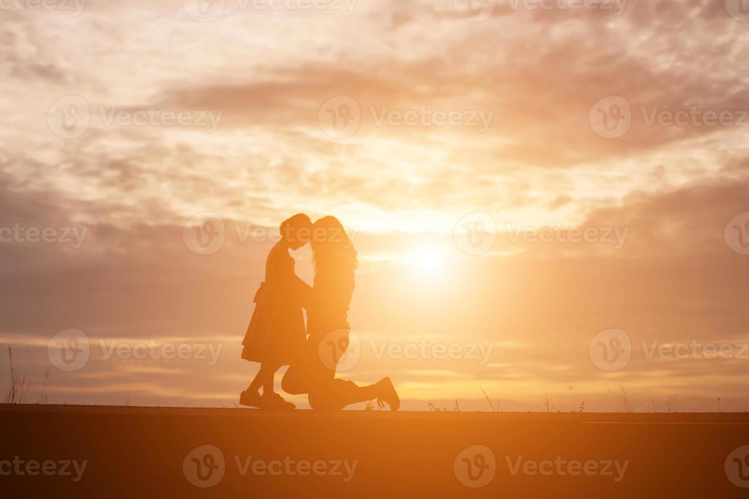 a silhouette of a happy young girl child the arms of his loving mother for a hug, in front of the sunset in the sky on a summer day. photo