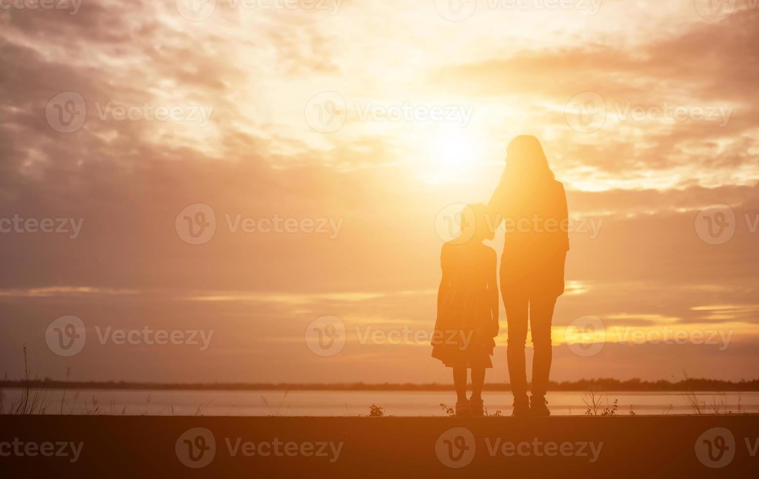 a silhouette of a happy young girl child the arms of his loving mother for a hug, in front of the sunset in the sky on a summer day. photo