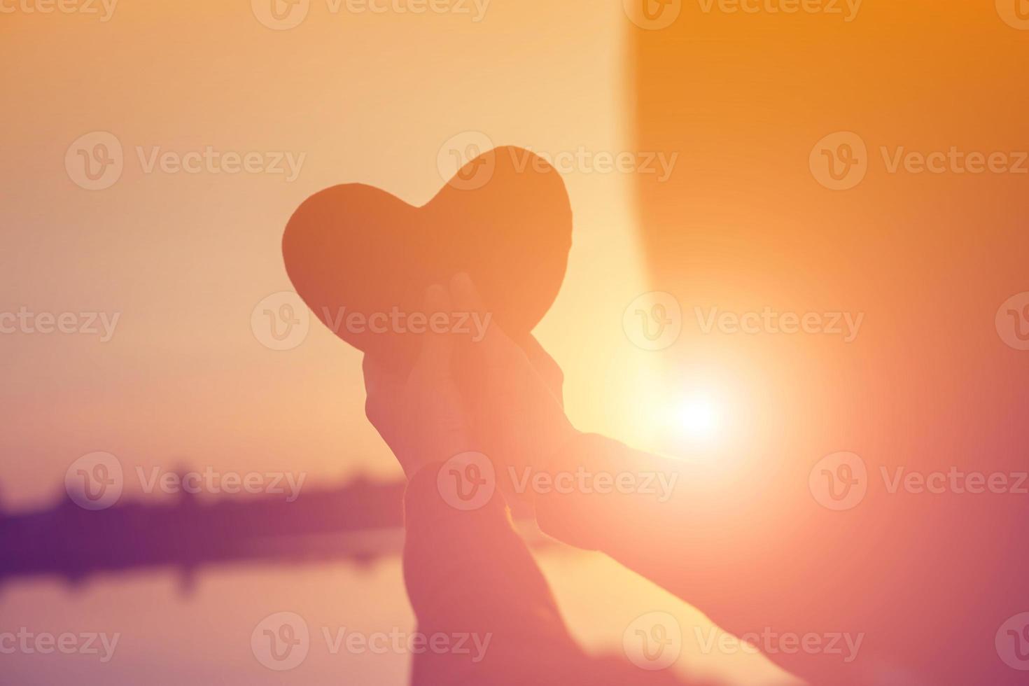 manos formando una forma de corazón con silueta de puesta de sol foto