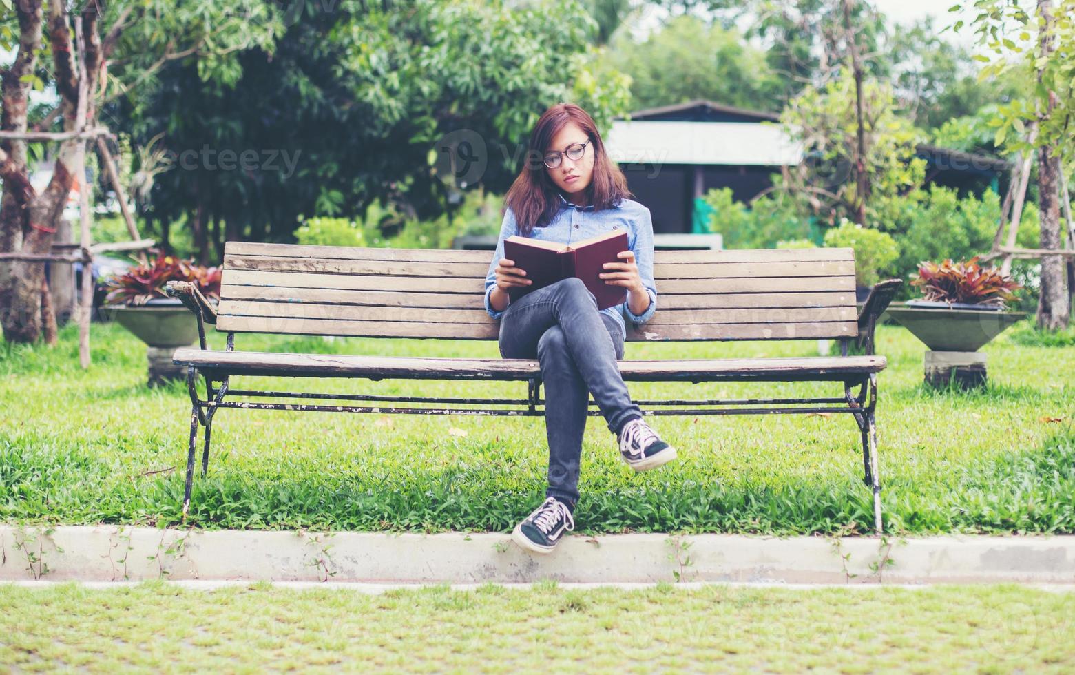 Hipster charming girl relaxing in the park while read book, Enjoy nature around. photo
