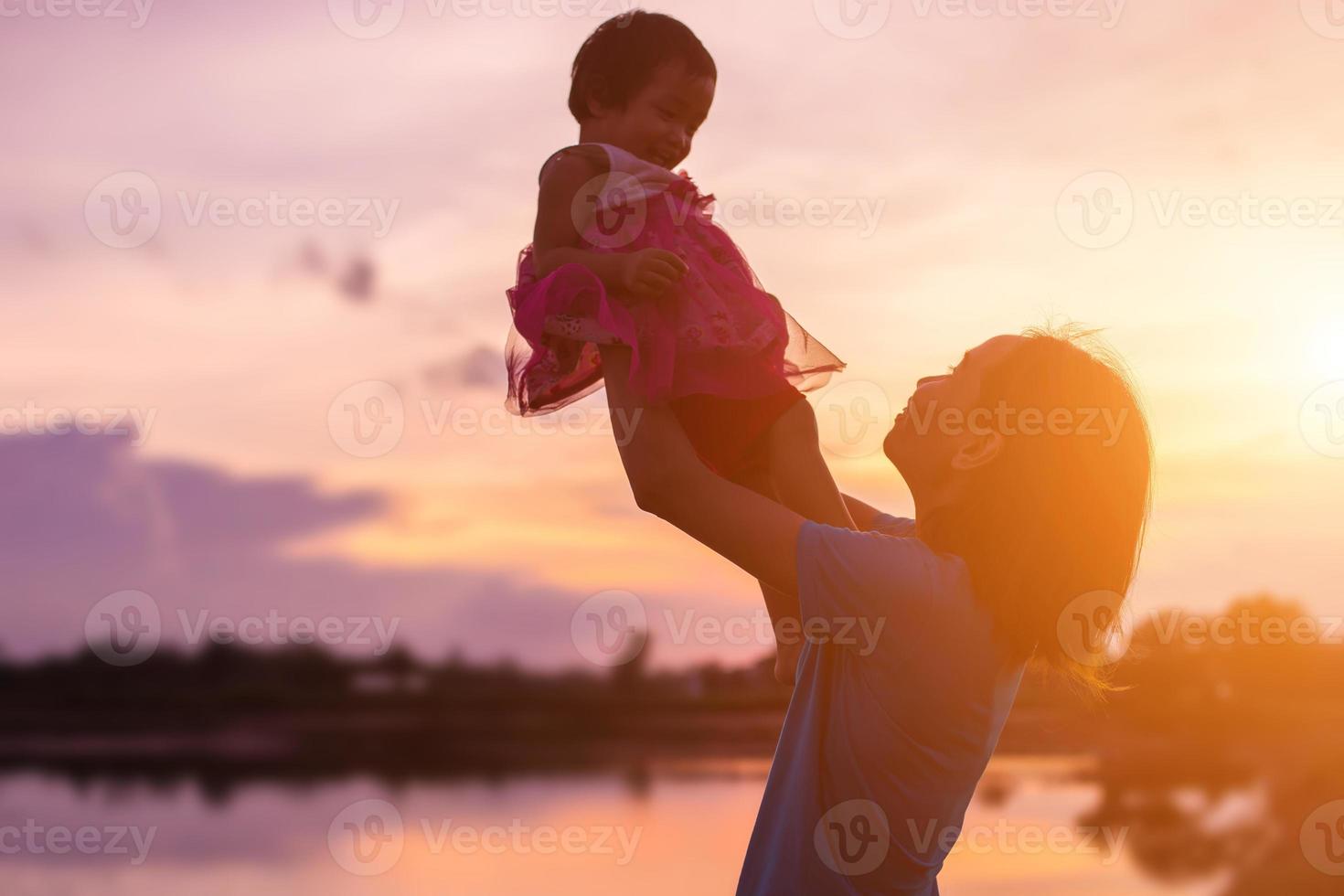 a silhouette of a happy young girl child the arms of his loving mother for a hug, in front of the sunset in the sky on a summer day. photo