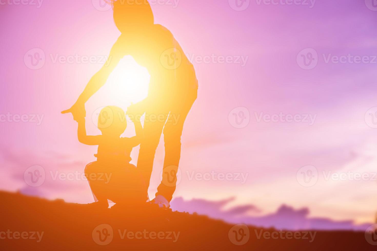 una silueta de una niña feliz los brazos de su madre amorosa para un abrazo, frente a la puesta de sol en el cielo en un día de verano. foto