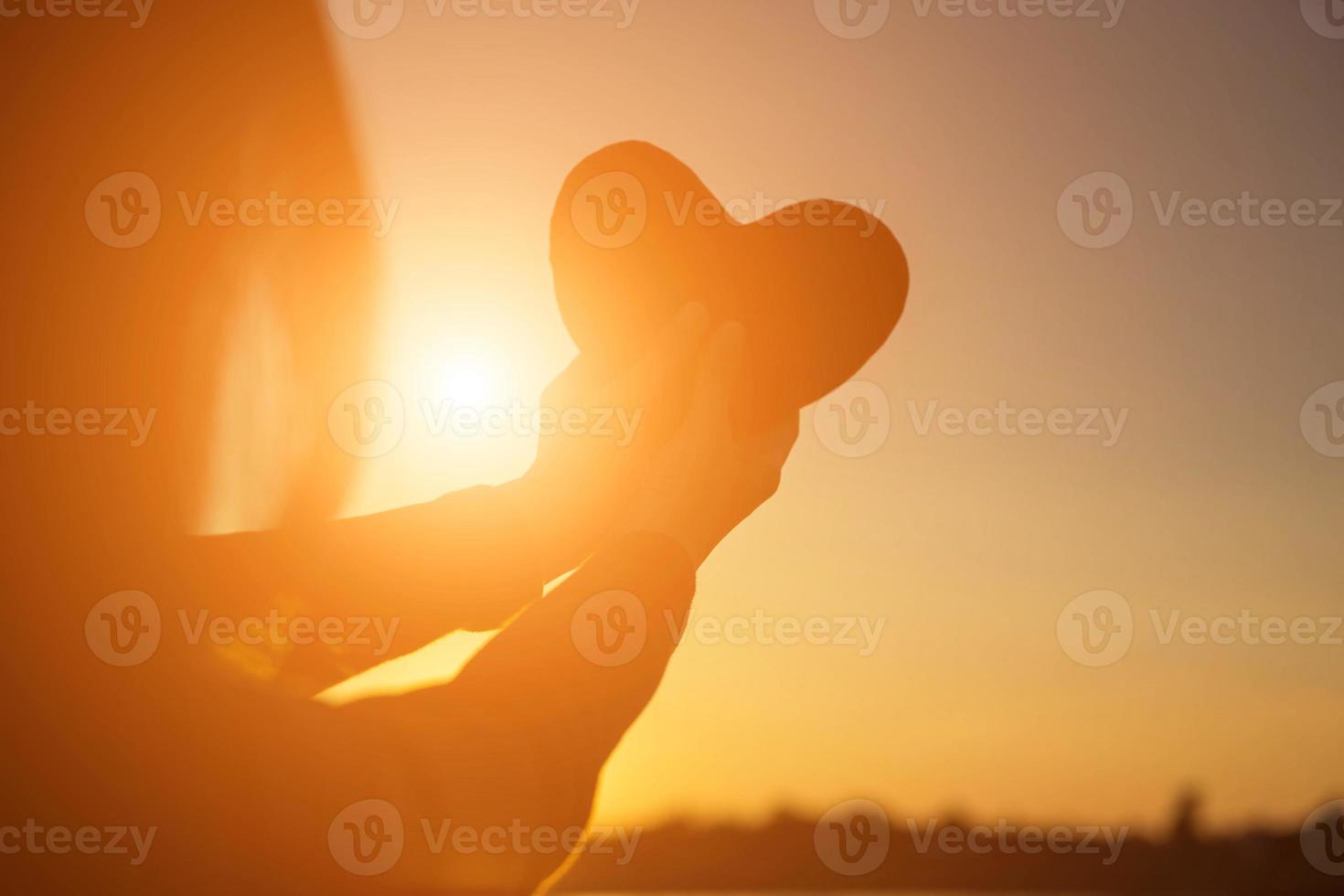 manos formando una forma de corazón con silueta de puesta de sol foto