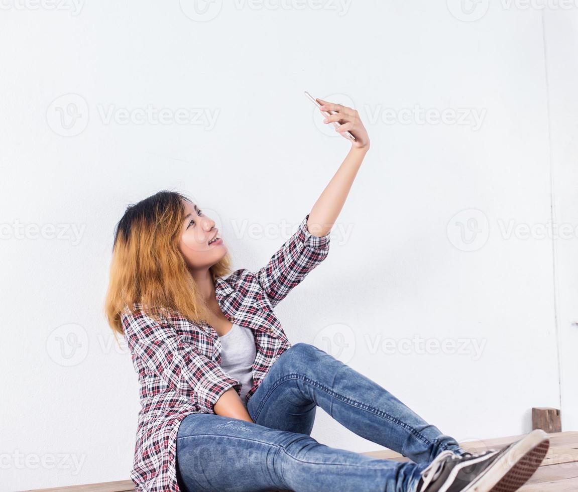 Happy young hipster woman taking selfie photo on smartphone over white background.