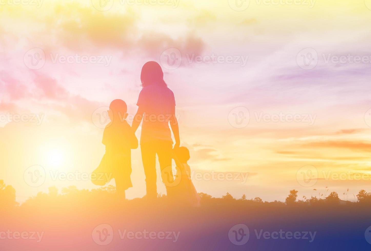 una silueta de una niña feliz los brazos de su madre amorosa para un abrazo, frente a la puesta de sol en el cielo en un día de verano. foto