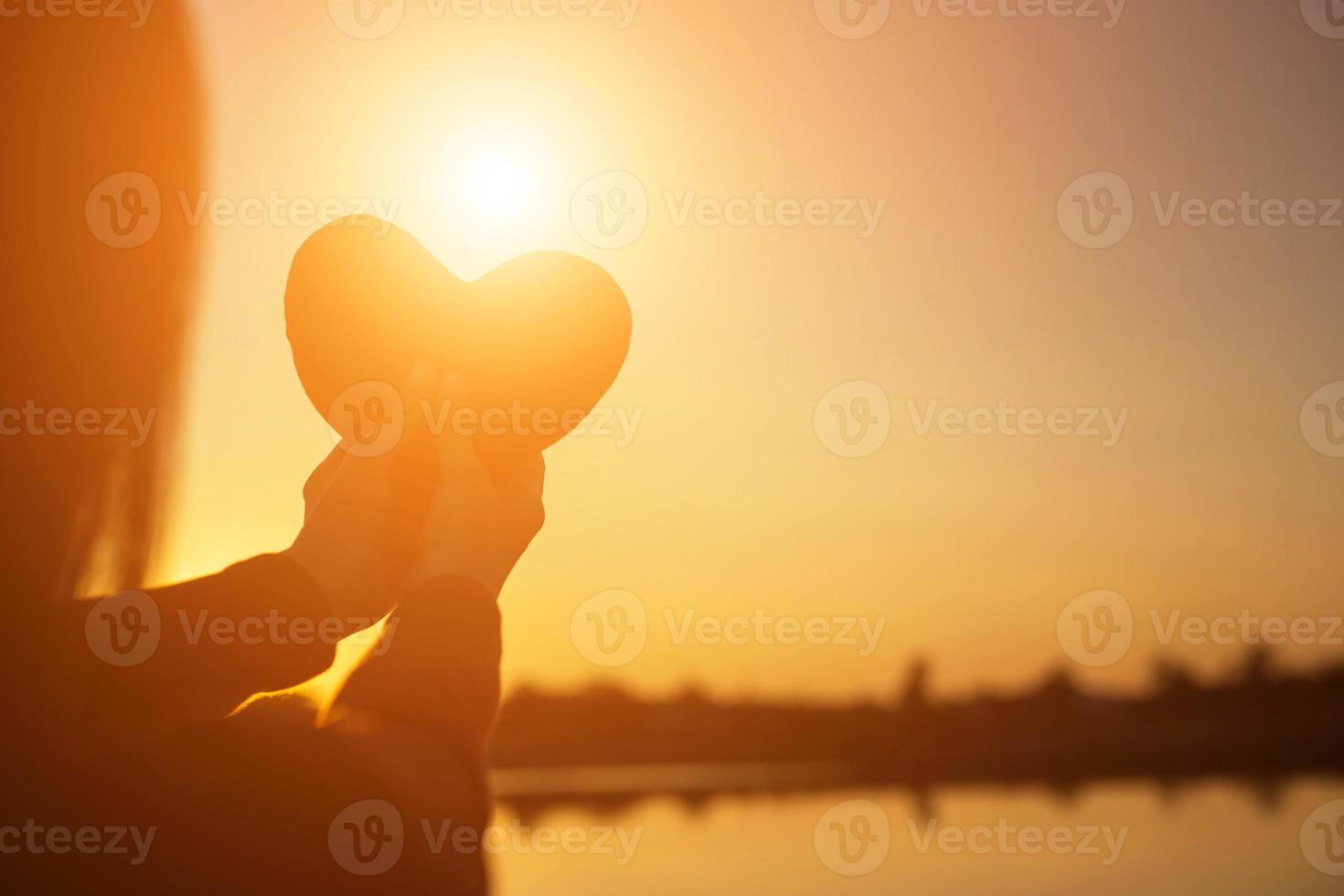 manos formando una forma de corazón con silueta de puesta de sol foto