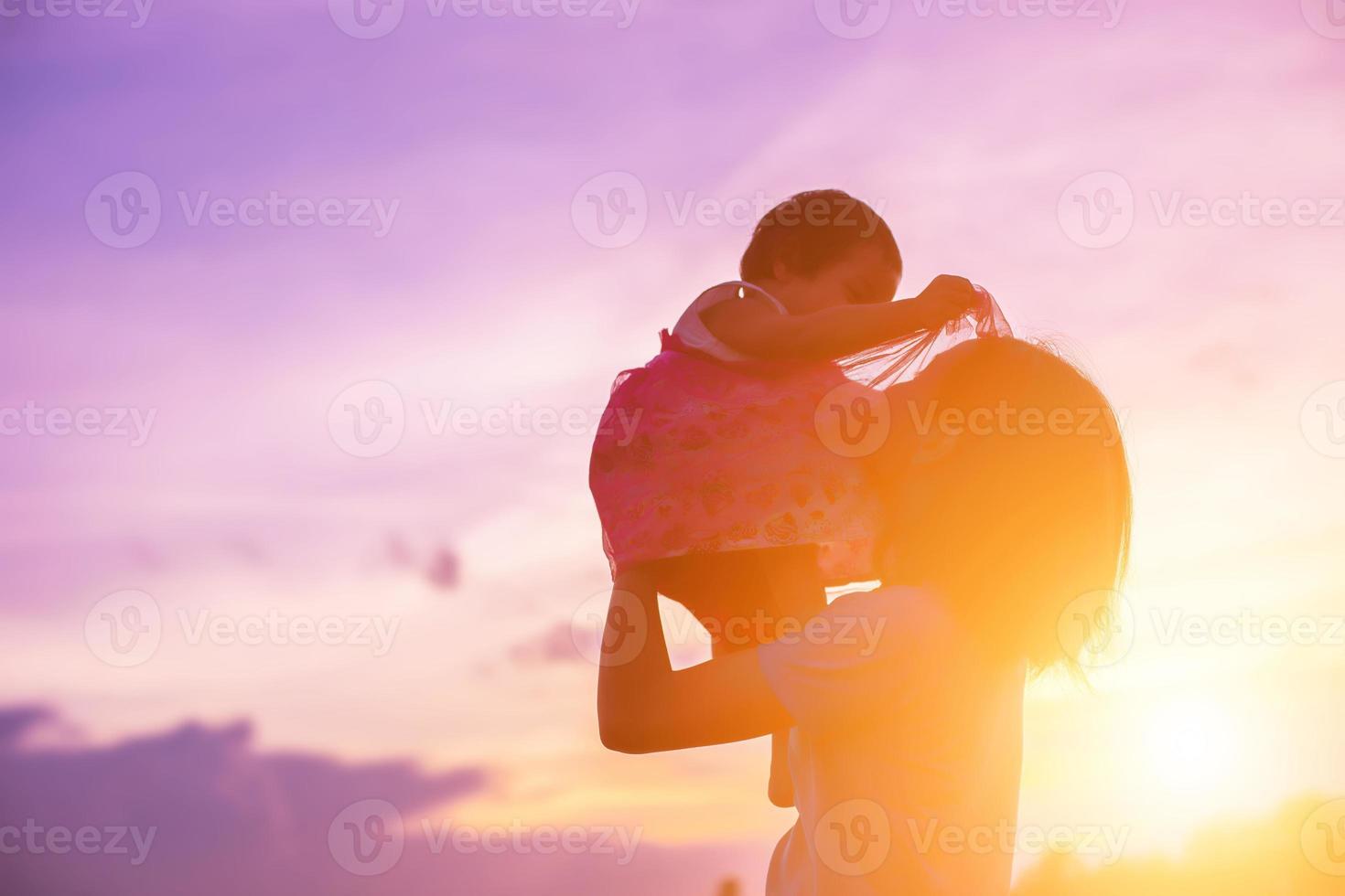 a silhouette of a happy young girl child the arms of his loving mother for a hug, in front of the sunset in the sky on a summer day. photo