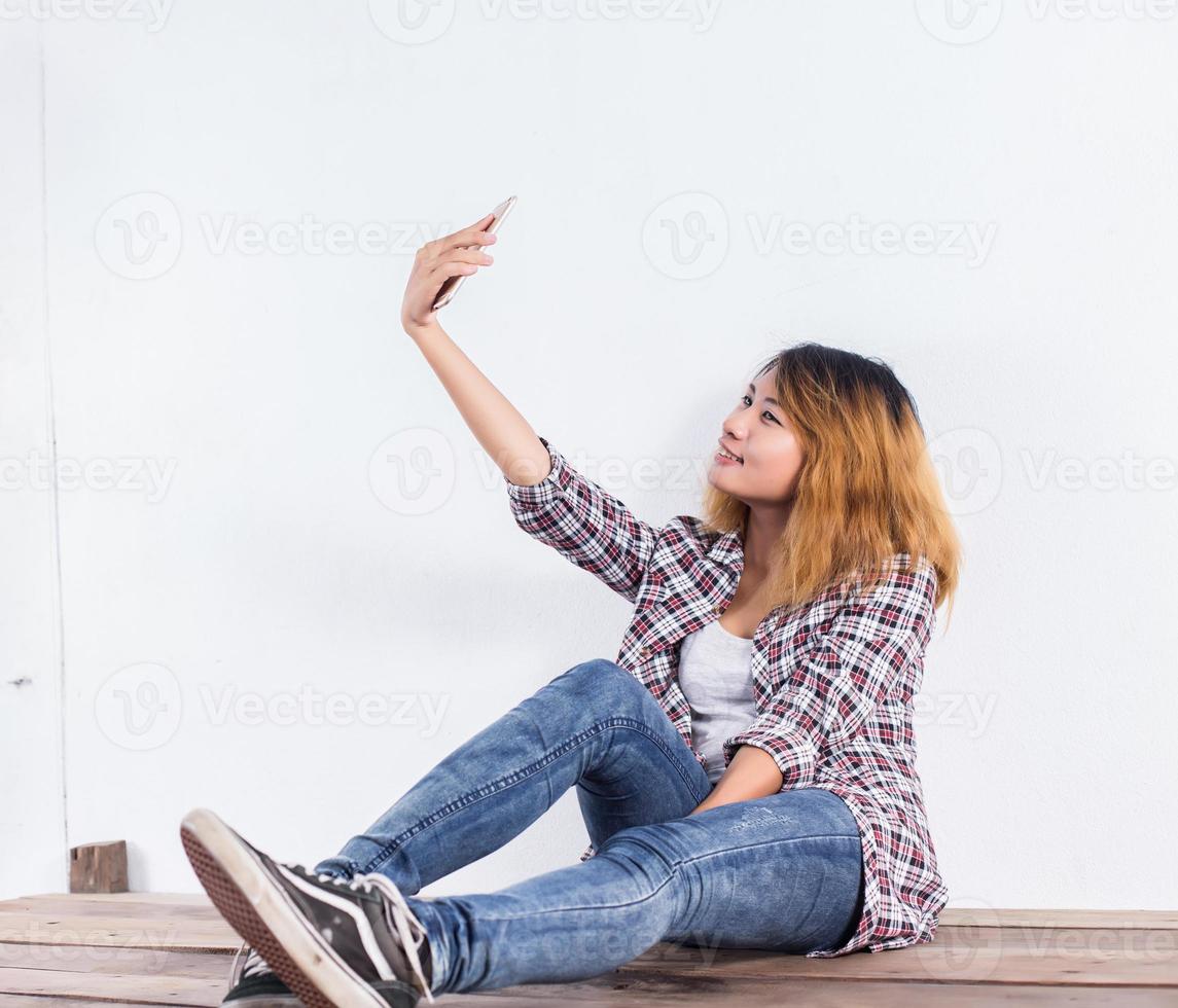 Happy young hipster woman taking selfie photo on smartphone over white background.