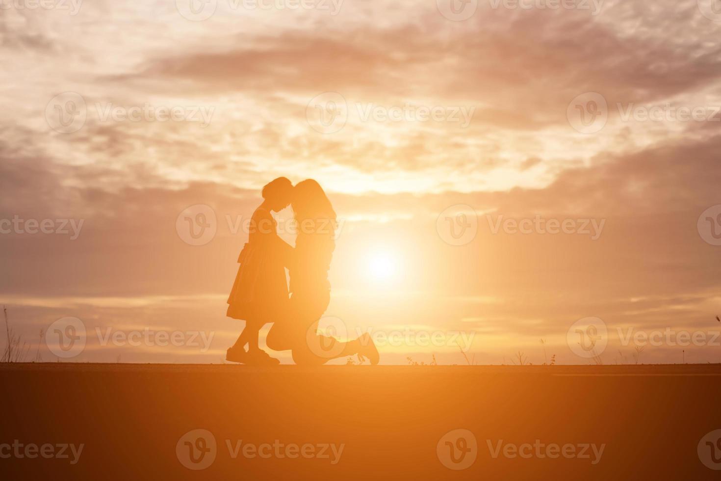 a silhouette of a happy young girl child the arms of his loving mother for a hug, in front of the sunset in the sky on a summer day. photo