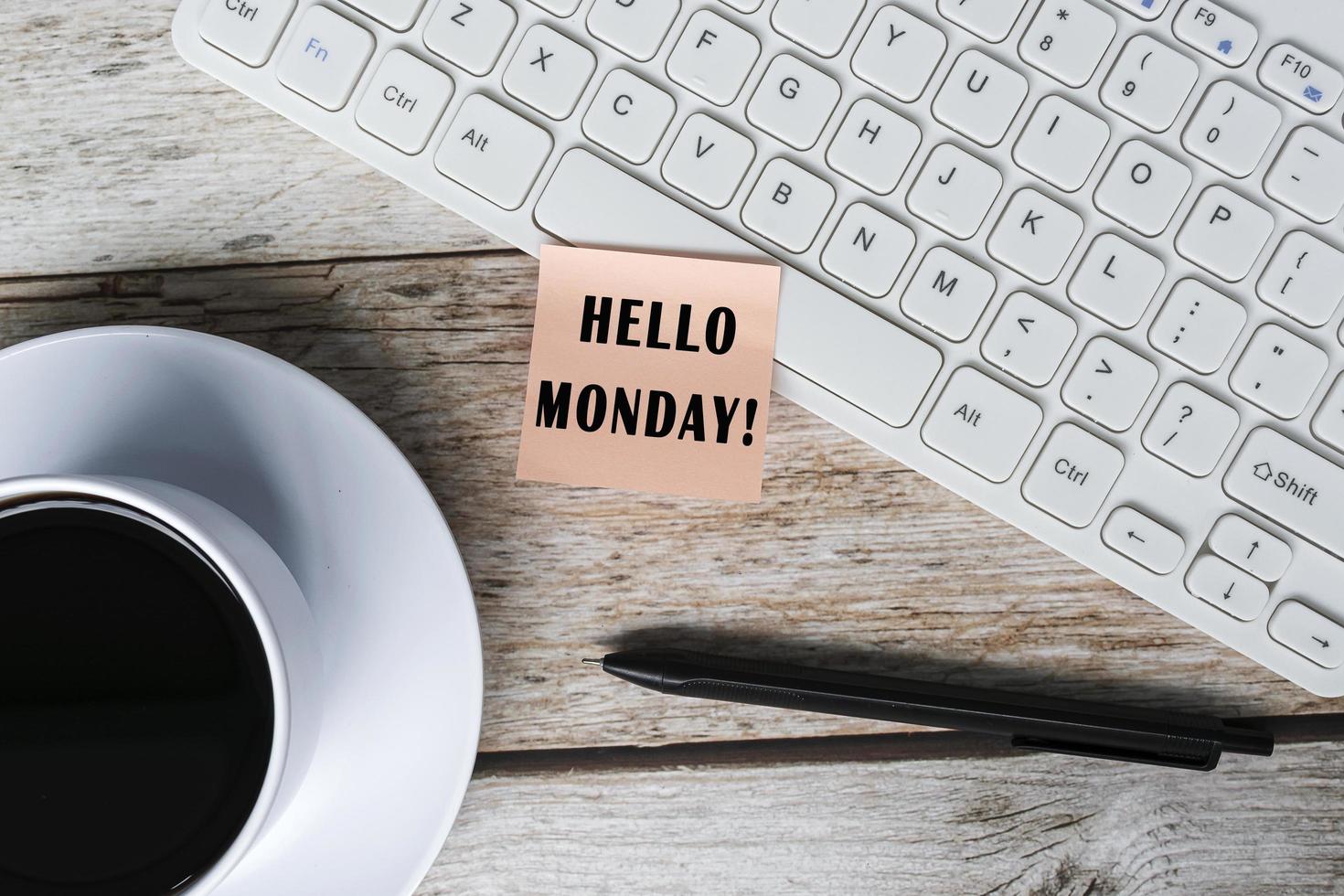 Note with hello monday stick on white keyboard on wooden desk with coffee. photo