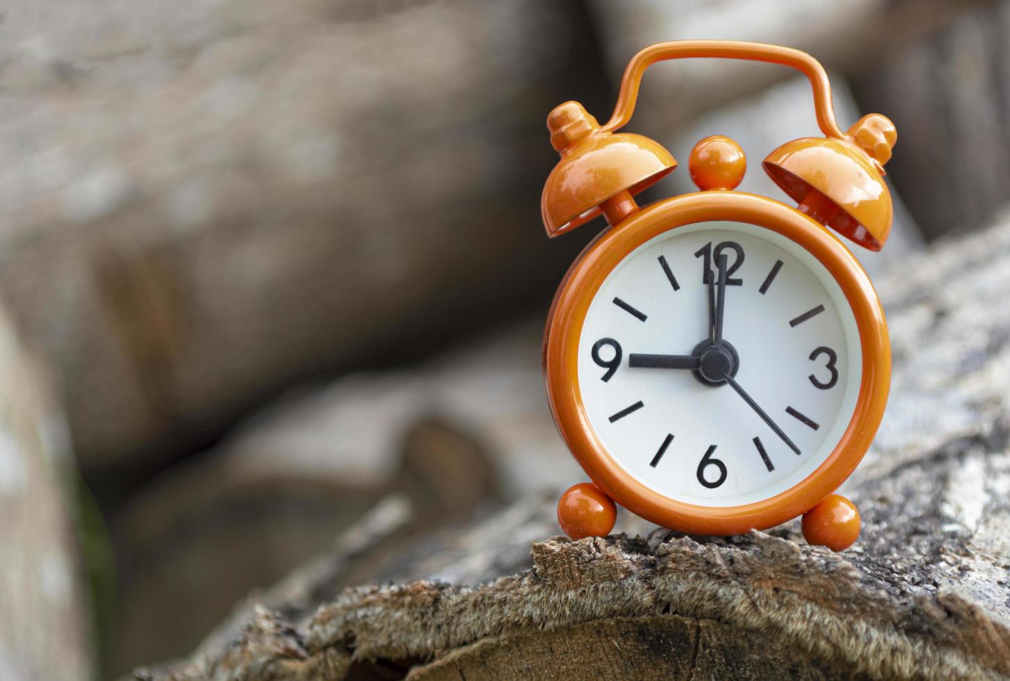 Orange alarm clock isolated on tree trunk. The clock set at 9 o'clock. photo