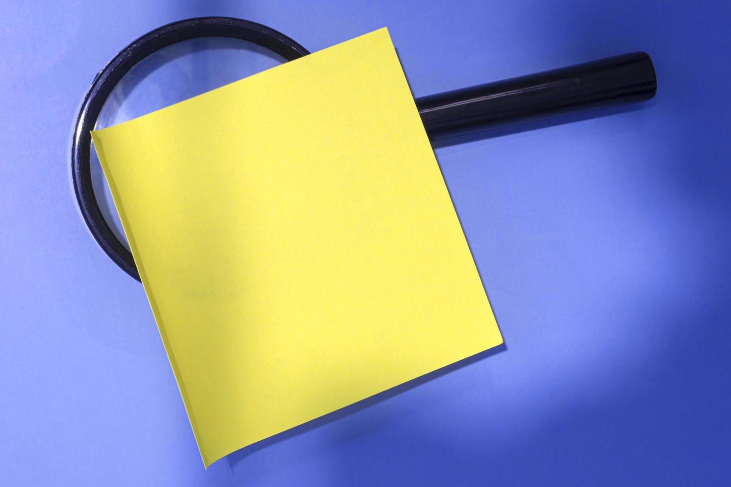 Adhesive Note With Magnifying Glass Against Blue background. Copy Space. photo