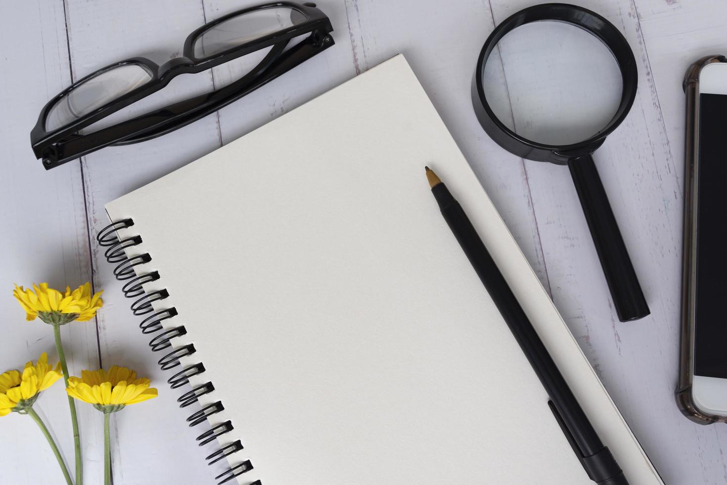 Note book with smartphone, magnifying glass, reading glasses, pen and sunflowers photo