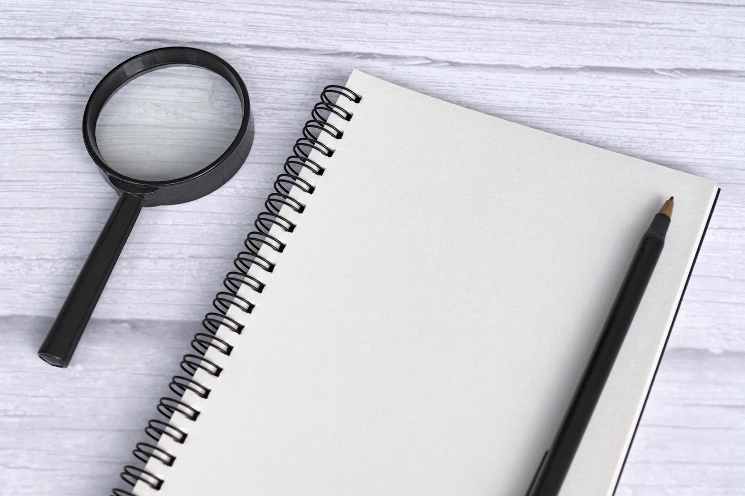 Note book flat lay with magnifying glass on white wooden desk. Directly above photo