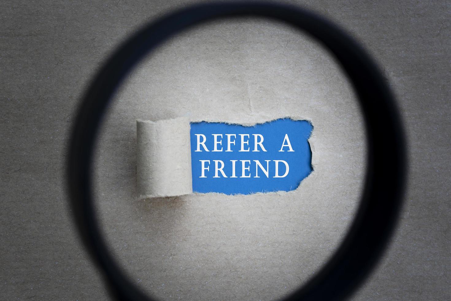 Refer A Friend text on torn paper with magnifying glass. Network concept. photo