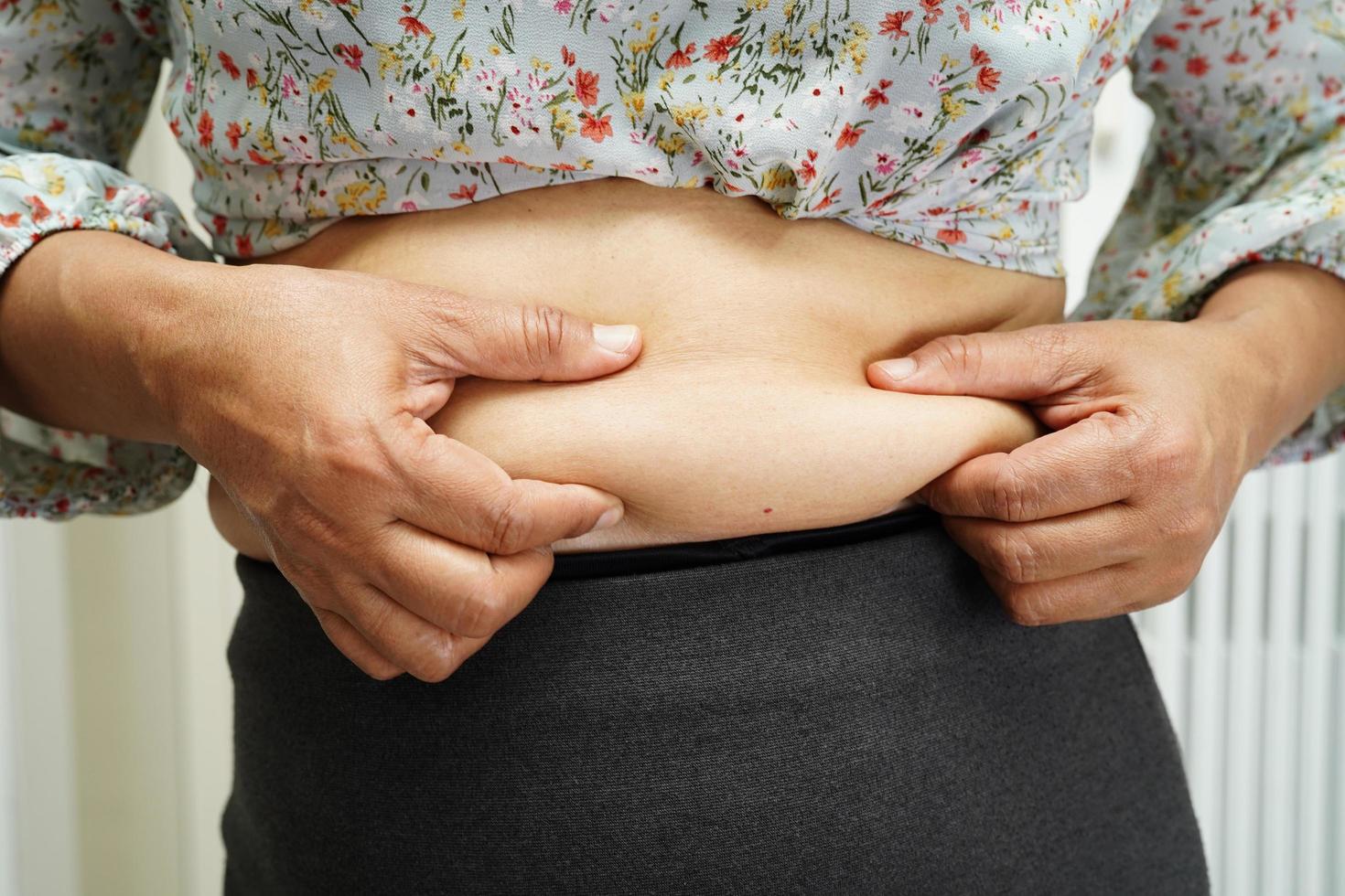 Overweight asian woman use hand to squeeze fat belly big size overweight and obesity. photo