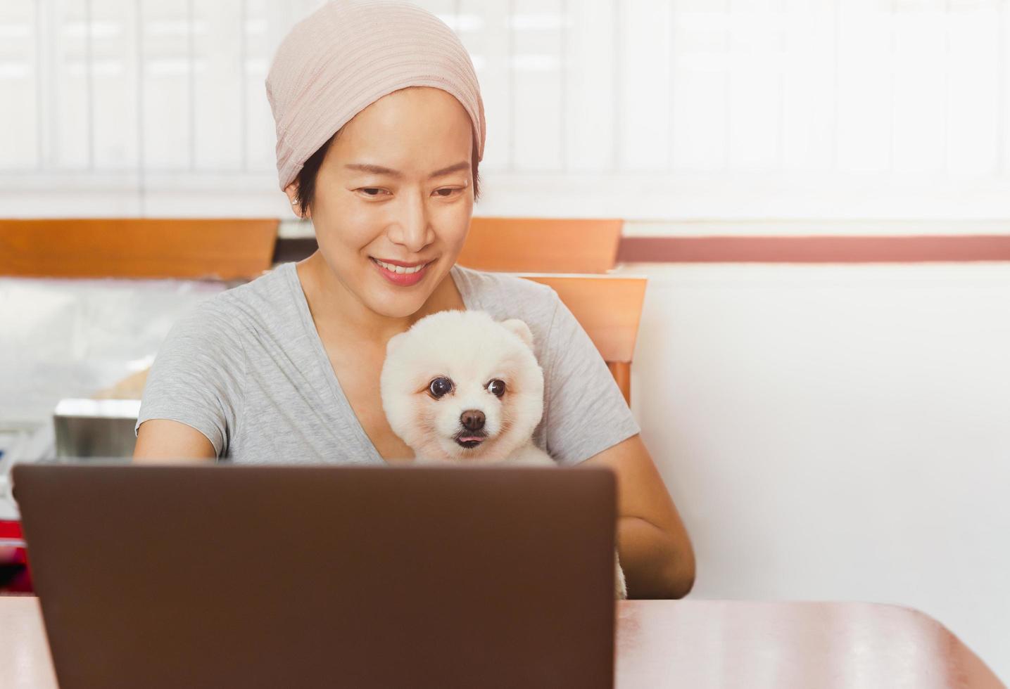 mujer independiente caucásica sosteniendo a su perro pomeraniano mientras trabaja en una laptop en casa. foto