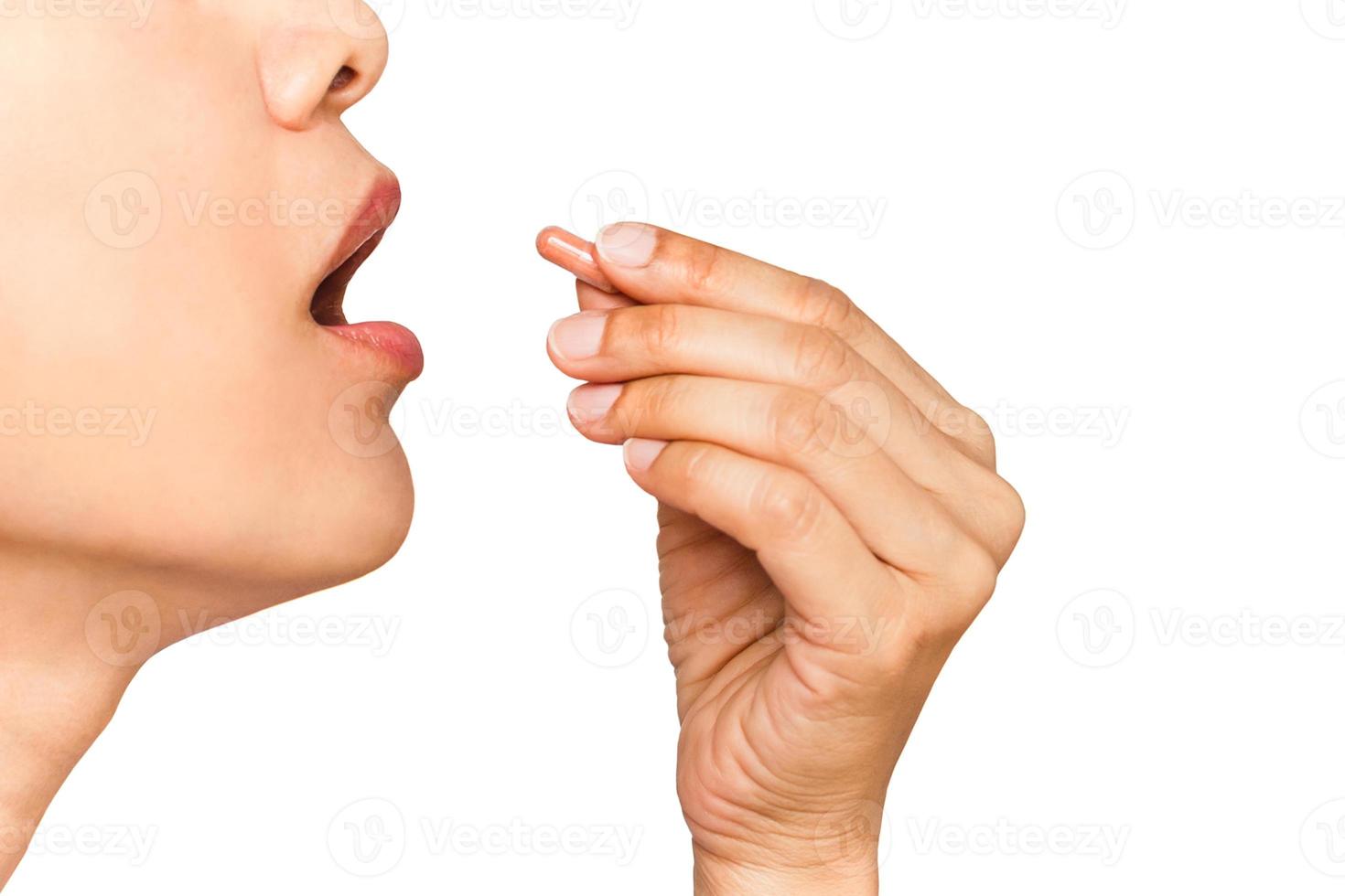 close up image of woman with her mouth open taking vitamin capsule isolate in white background. photo