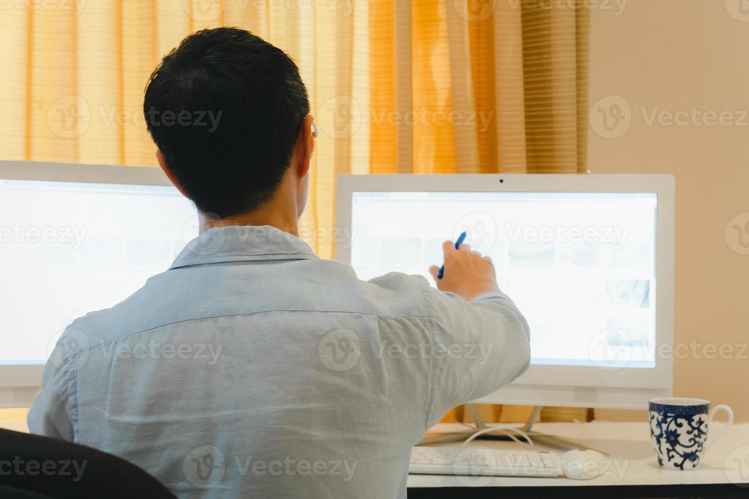 Back View of man working on Pc computer sitting at desk at home office. photo