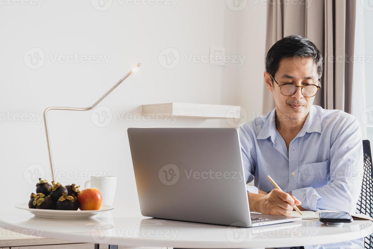 hombre de negocios maduro escribiendo notas en la agenda mientras trabaja en una computadora portátil en casa. foto