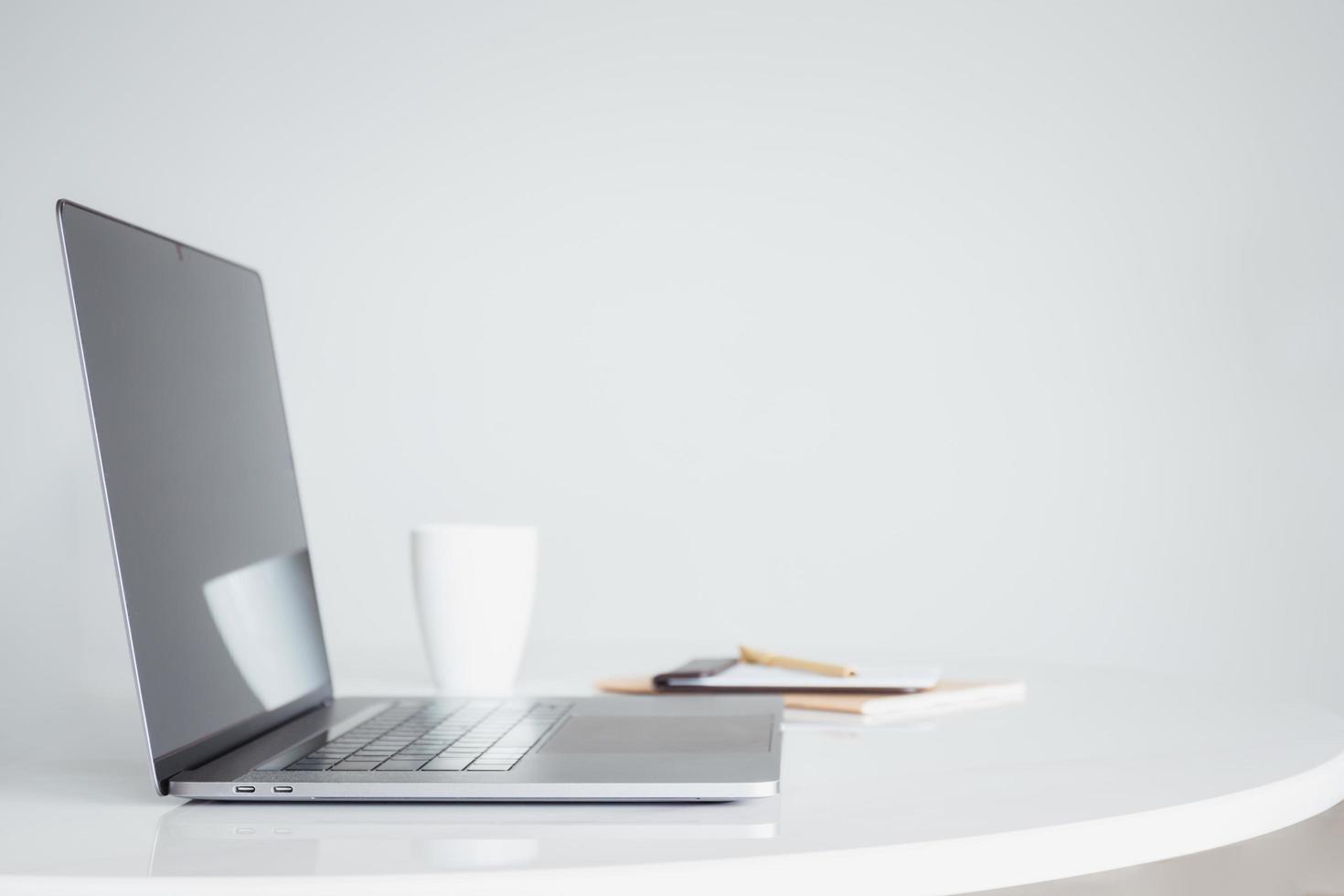 Open laptop computer with coffee and notebook on white table. photo