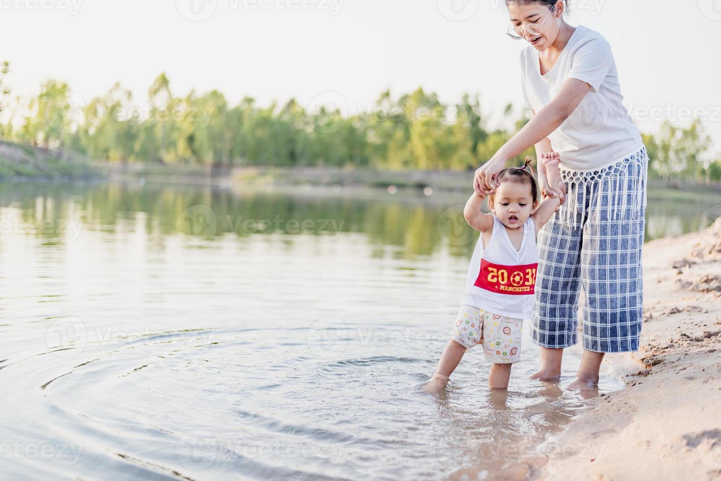 A young mother plays with her 2-5 year old daughter on the beach in summer. Outdoor resort on the lake Have a good rest on weekends, family days. photo