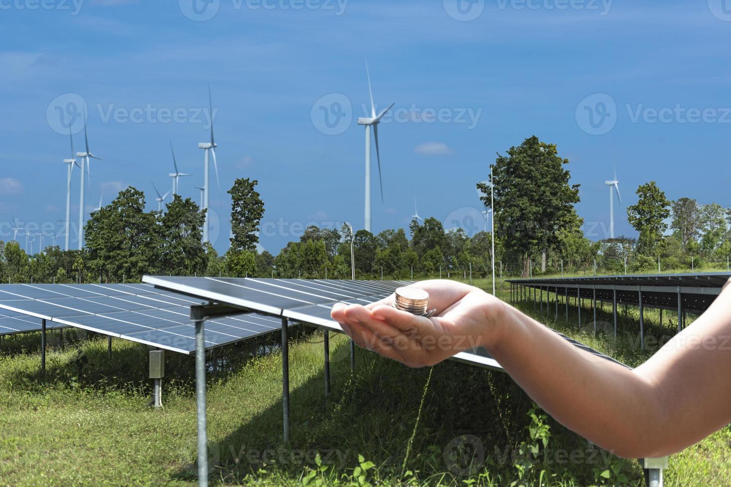 Renewable Energy Economics Money in the palm of your hand in front of solar panels and wind turbines. Three-dimensional illustrations. photo