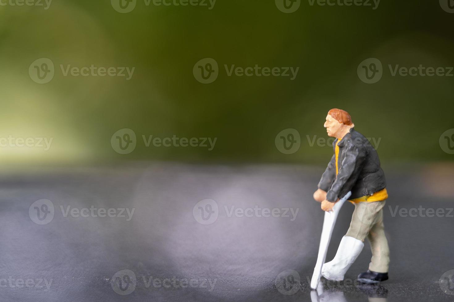 Miniature people man with broken leg is using crutch For Walking photo