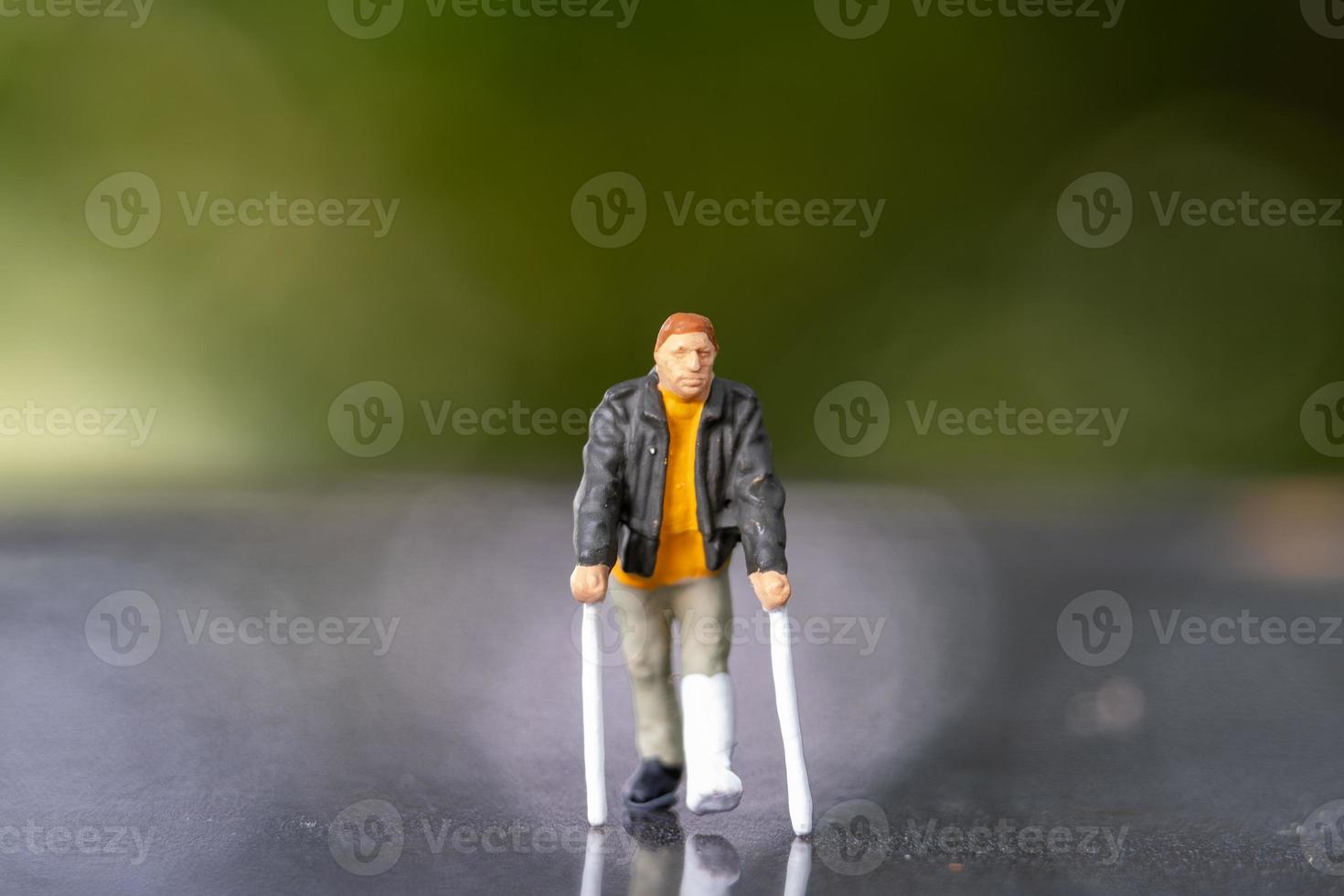 Miniature people man with broken leg is using crutch For Walking photo