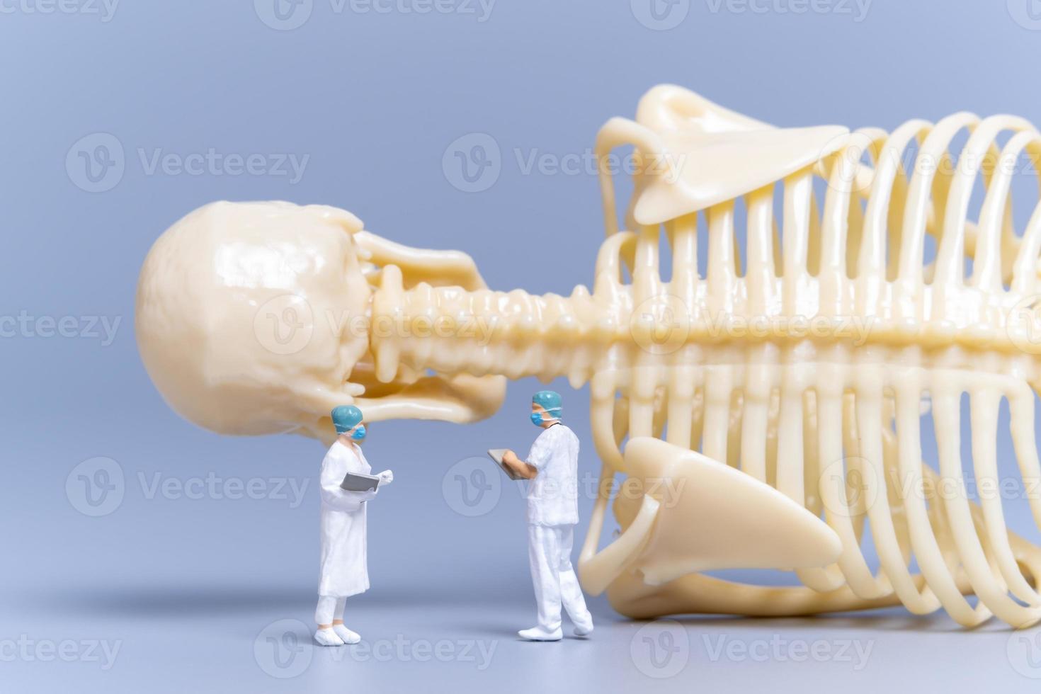 médico de personas en miniatura con un hueso humano gigante sobre un fondo gris foto