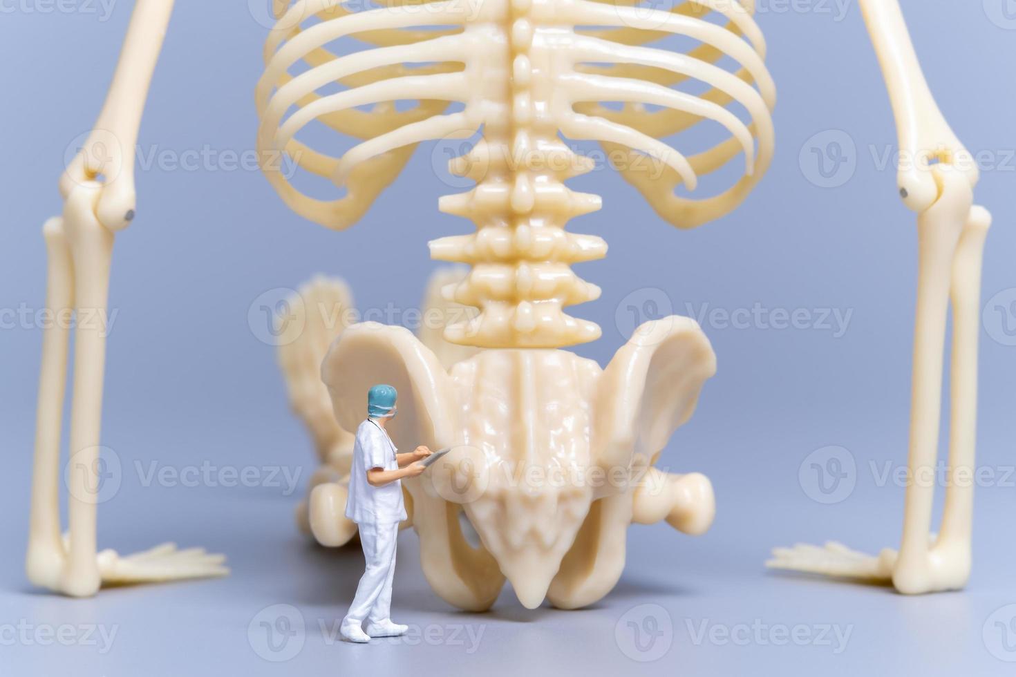 médico de personas en miniatura con un hueso humano gigante sobre un fondo gris foto