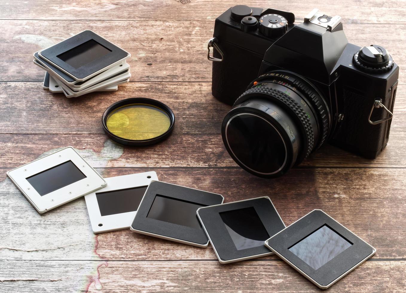 Vintage camera with yellow filter and slides on wooden background. Retro style technology photo