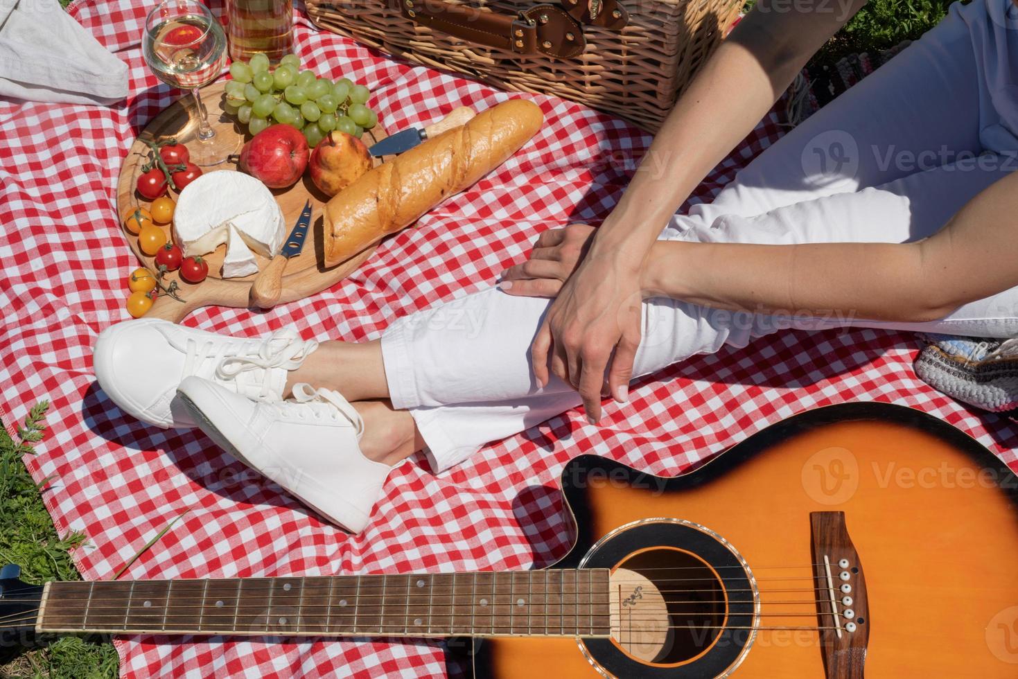 Top view of unrecognizable young woman in white pants outside having picnic, eating and playing guitar photo