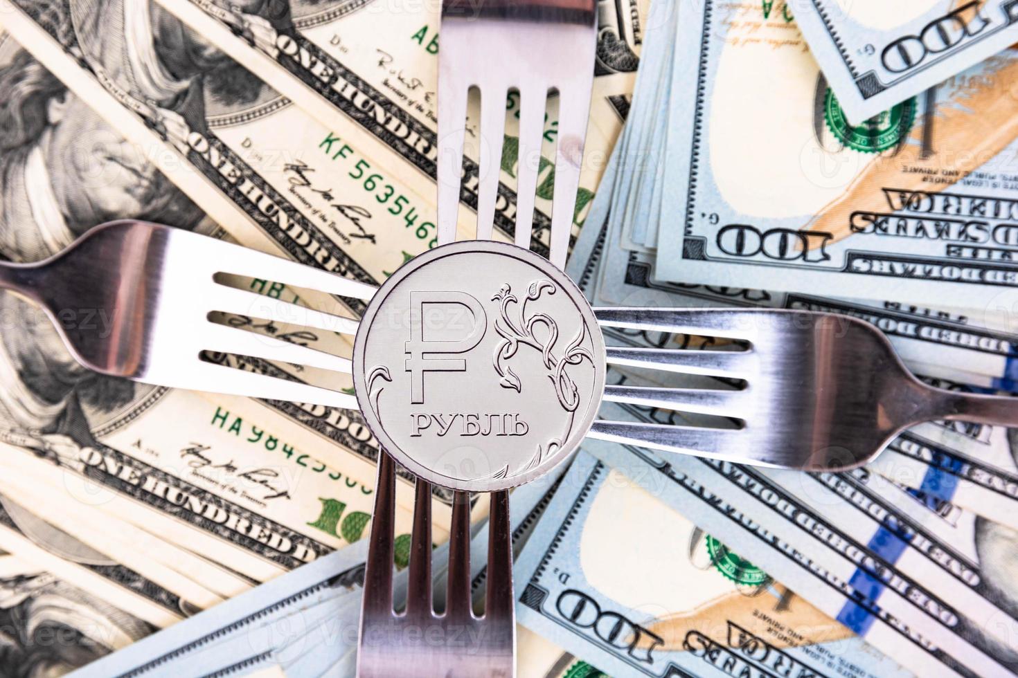 A new metal coin of the Russian ruble, with a denomination of one ruble against the background of American banknotes and metal forks. Crisis in Russia. photo