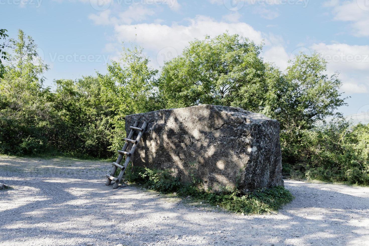 A large, huge stone megalith with a staircase against the background of green trees and a blue sky, used as an observation deck. photo