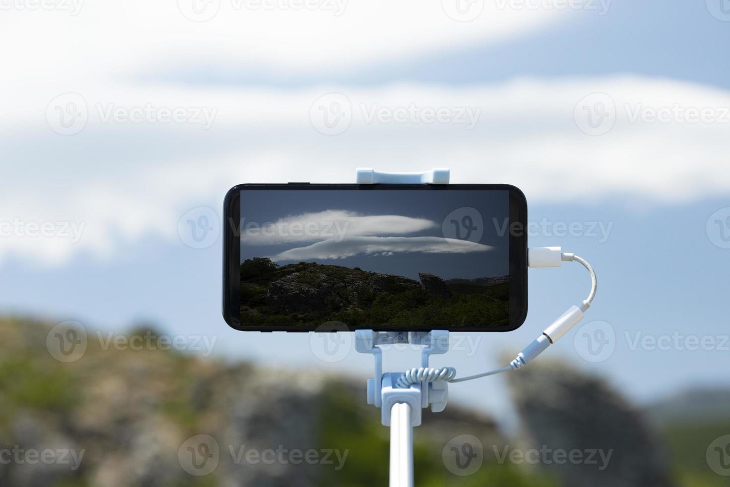 A smartphone on a selfie stick photographs a rare phenomenon, the Lenticular cloud. Mobile photography while traveling. photo