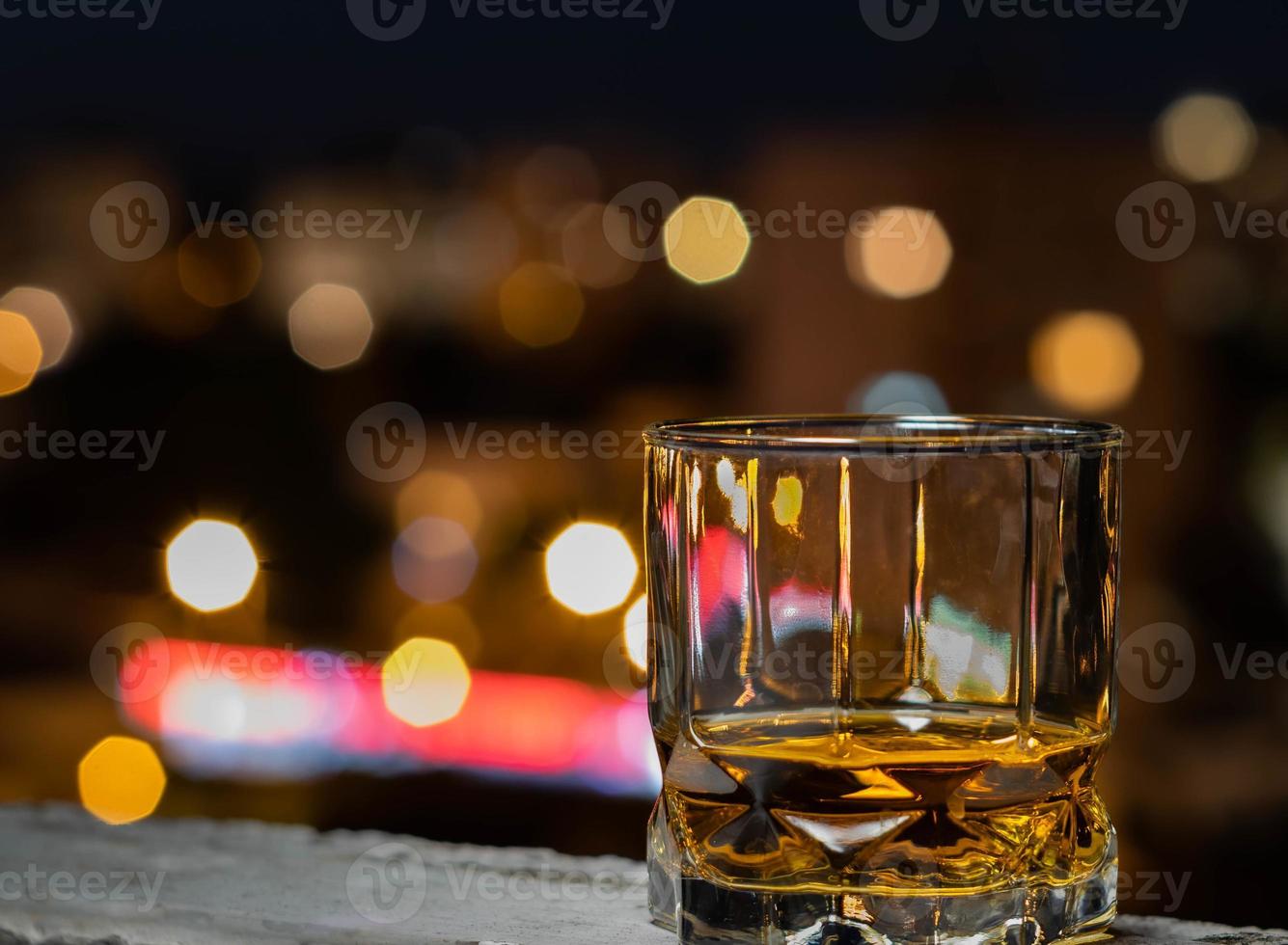 whisky de malta en un vaso de whisky en una noche de verano con el bokeh de la ciudad en el fondo foto