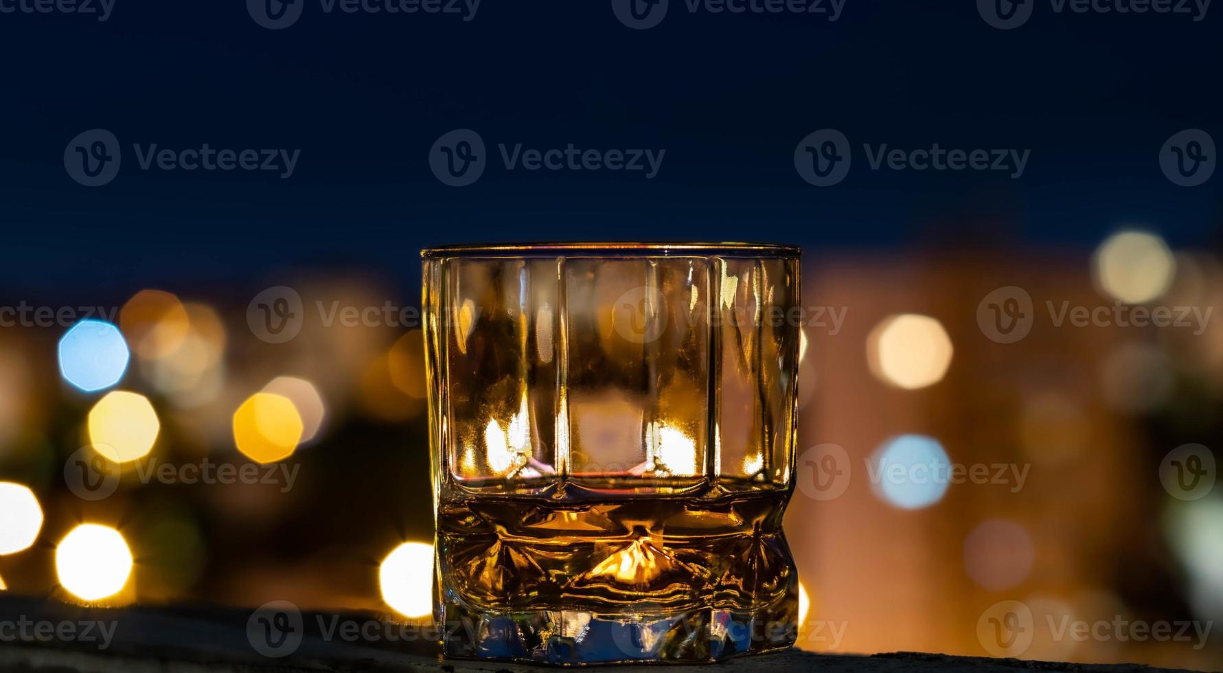 whisky de malta en un vaso de whisky en una noche de verano con el bokeh de la ciudad en el fondo foto