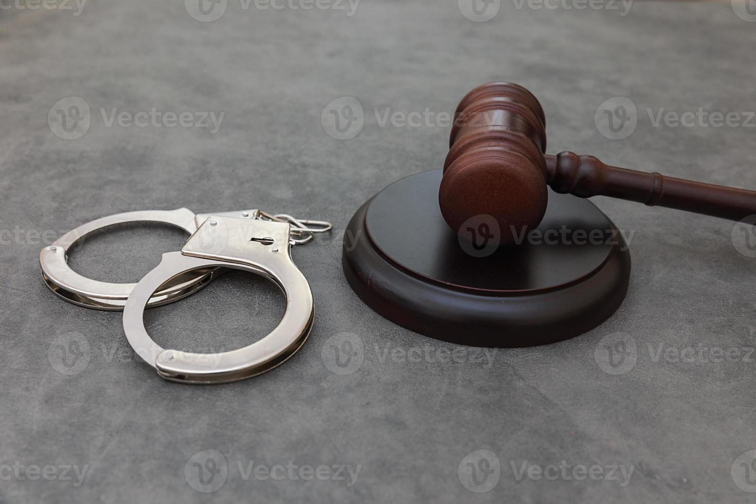 Law theme. Court of law trial in session. Judge gavel handcuffs on grey table in lawyer office or court session. Mallet of judge on concrete stone grey background. Justice human rights concept. photo