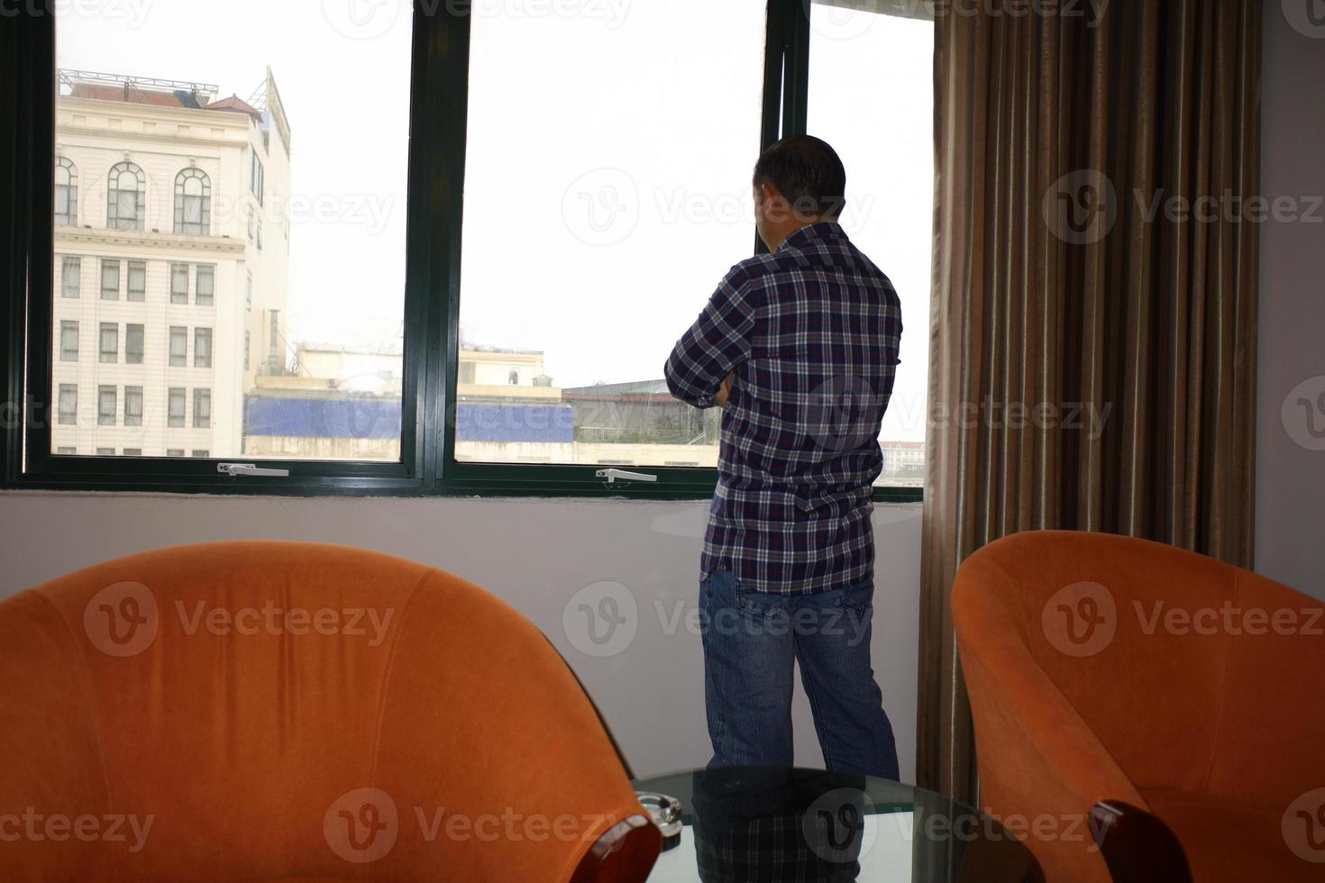 un hombre guapo de pie y mirando a través del balcón del dormitorio visto a través de un concepto de viaje o negocio de ventana de vidrio. foto