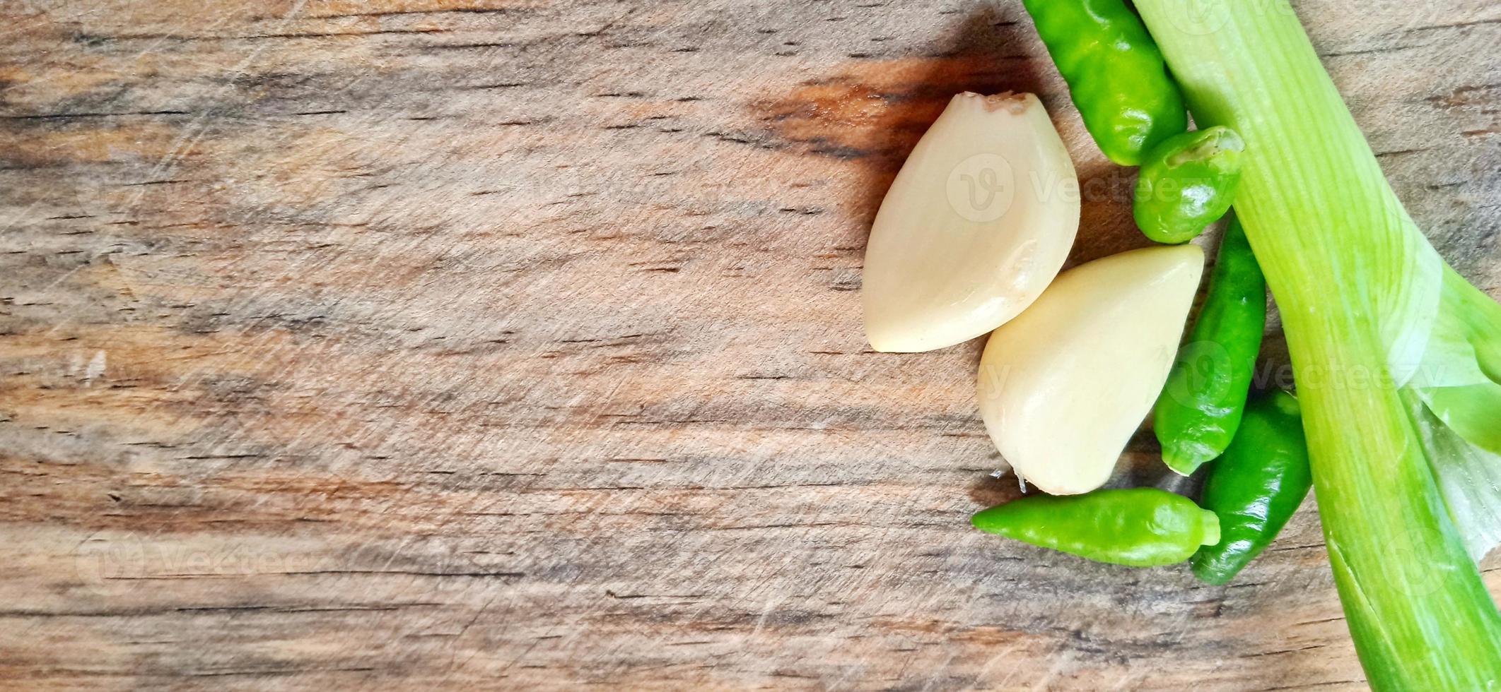 Vegetables of leek, garlic, and green chilli on the wooden cutting board. Vegetables ingredient background design. Suitable for advertising of food, drink, poster, backdrop, food company and industry. photo